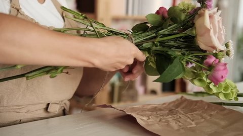 Professional floral artist, florist binding of stems at flower shop, workshop.  Female florist preparing bouquet. Floristry, handmade and small business, entrepreneurship concept. Close up