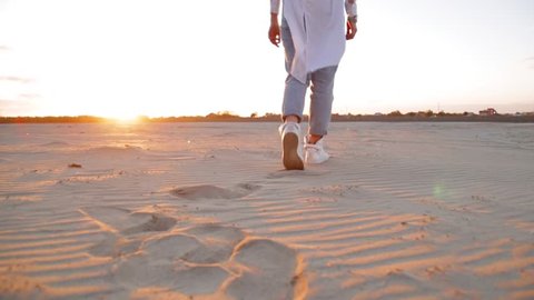 A woman walking in the sand at sunset
