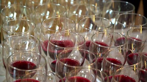 The waiter pours red wine in the rows of glasses at the festival. On the table is a bunch of red glasses. Wine tasting.