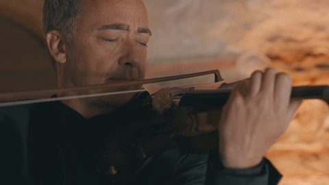 Close up shot of an older male violinist playing a long note on his violin