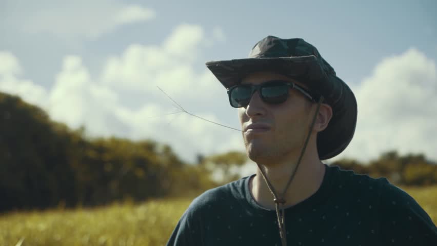 Close up shot of a young millennial guy chewing on a twig of long grass while standing in a field in Bali
