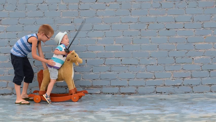 Amusing child rolling his younger brother on toy rocking horse with plastic sword. Boy dreams of battles, victories and adventures.Concept of moral education, patriotism, hero, super. Children happy Royalty-Free Stock Footage #1013946965