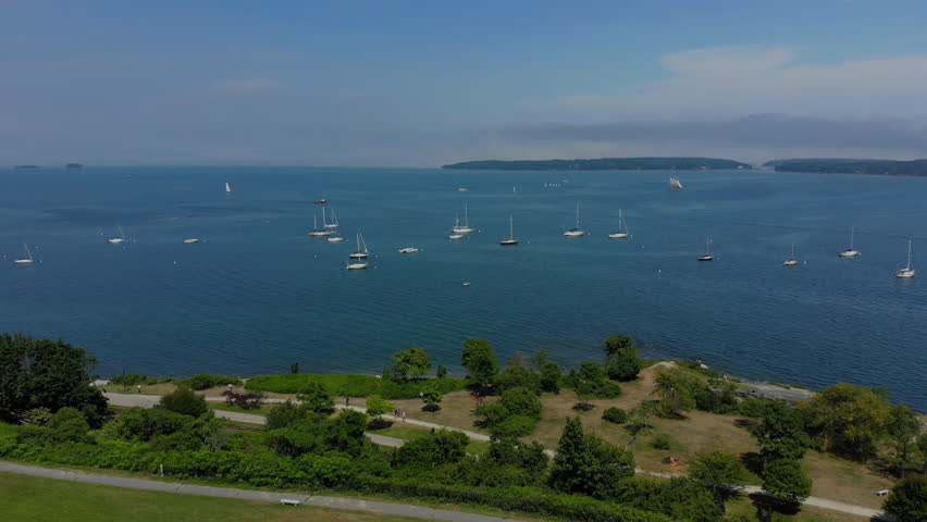 A reverse aerial view of Fort Allen Park in Portland, Maine on a summer foggy day. Boats and Fort Gorges on the Fore River harbor in the distance.  	