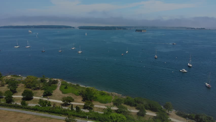 A laterally moving aerial view of Fort Allen Park in Portland, Maine on a summer foggy day. Boats on the Fore River harbor and Fort Gorges in the distance.  	