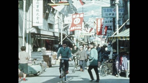 1950s JAPAN: People walk and ride bicycles through vendor street in Osaka. Man demonstrates abacus to customers. Bunraku theater.