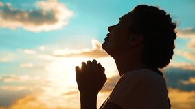 girl praying. girl folded her hands in prayer silhouette at sunset. slow motion video. Girl folded lifestyle her hands in prayer pray to God. asks forgiveness for sins of repentance. believing girl