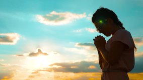 Girl folded her hands in prayer silhouette at sunset. slow motion video. Girl folded her hands in prayer pray to God. girl praying asks forgiveness for sins lifestyle of repentance. believing girl