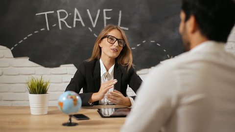 Smiling bright travel agent having meeting with client, attractive young woman talking to handsome bearded man about possible countries to visit, indoor shot in black and white office