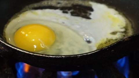 An egg white and yolk frying sunny side up in a pan on open gas flame sizzling and popping to a crisp healthy breakfast protein treat.  No carb diet friendly option for nutrition to feed the body 