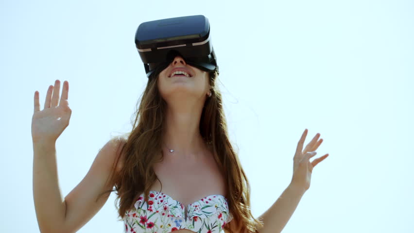 Beautiful young female playing game in vr glasses on the beach. Girl with pleasure uses head-mounted display outdoors. Royalty-Free Stock Footage #1013976533