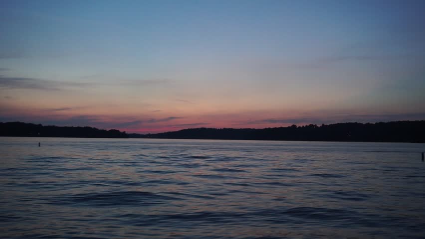Pretty natural colors created from earths layers and atmosphere with clouds and sky above beautiful flowing waves of lake water creating a inspiring relaxing scene to end the fun summer day of boats 