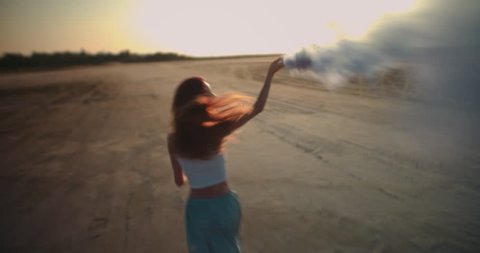 Young woman running with smoke bomb and celebrating at music festival in desert
