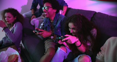 Happy multi-ethnic teenage friends relaxing on living room sofa and playing video games