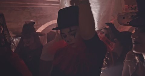 Woman in evil clown costume and scary make-up dancing at Halloween nightclub party with friends