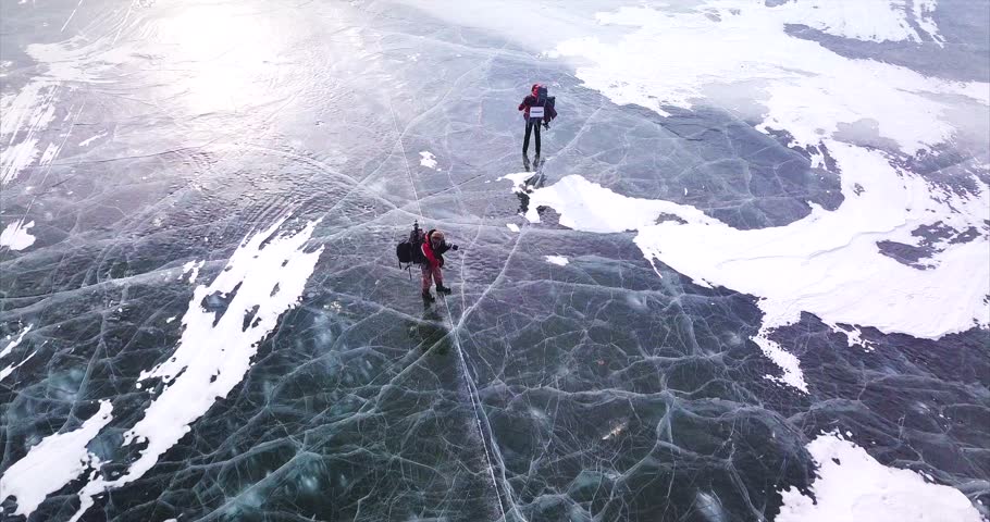 Aerial view of frozen lake and two photographers of wild nature with photography equipment walk along the ice. Lake Blagodatnoe in the Sikhote-Alin Biosphere Reserve in Russia