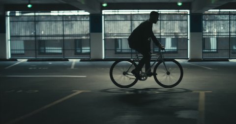 TRACKING Handsome young adult man wearing suit checking phone before riding his classic bicycle to work through an empty parking garage. 4K UHD 60