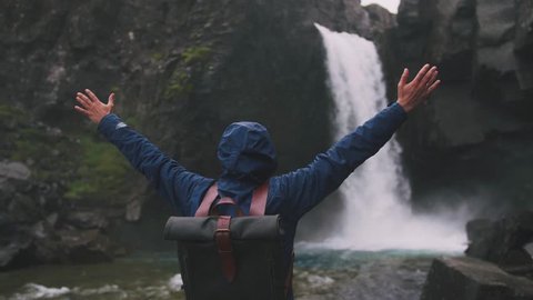 Back view shot of young man rising hands near the powerful waterfall in Iceland, cinematic shot