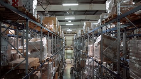 A large warehouse with boxes of goods. The camera moves up along the shelves with cardboard boxes. A forklift works in the distance
