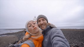 Girl blowing a kiss, Travel couple taking selfie at lighthouse in Gardur town near Reykjavik city in Iceland. Springtime cold temperatures vacations fun concept. Slow motion HD format 1080p