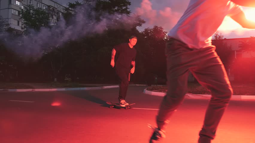 Group of young people skateboarding on the road in the early morning with red signal flare, slow motion Royalty-Free Stock Footage #1013994971