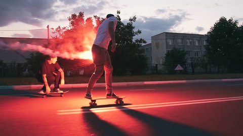 Group of young people skateboarding on the road in the early morning with red signal flare, slow motion
