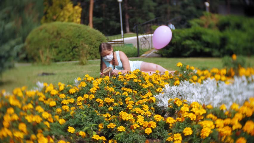 Cute girl in a respirator reading a book in the park 4k