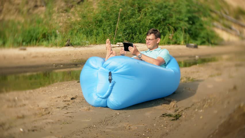A man is resting on an inflatable mattress by the sea. He uses a tablet 4k