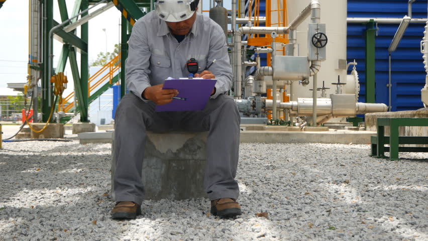 Engineer sitting at outdoor factory and checking machine specification paper on clipboard