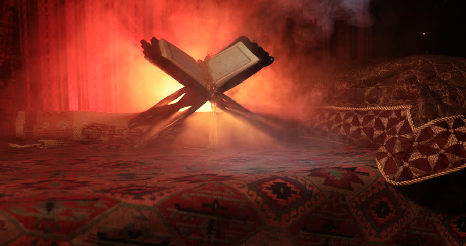 Open holy book of Muslims on stand on eastern carpet with dark toned foggy background. Muslim religion concept. Selective focus. Slider shot. | Shutterstock HD Video #1014011894