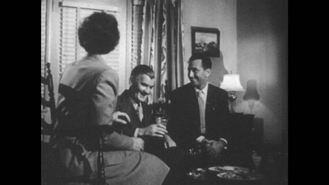 1950s: Man talks to family. Man rises from chair and shakes man's hand.