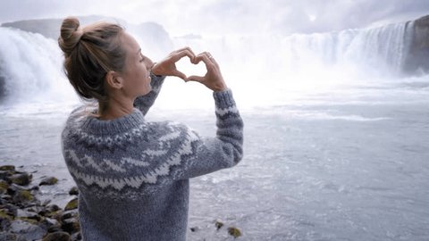 Young woman in Iceland making heart shape finger frame on spectacular waterfall loving the beauty in nature, tourism travel people concept in Northern Europe countries 4K