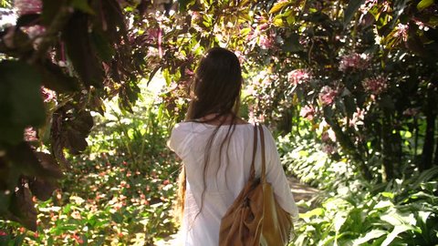 Following a beautiful woman walking between tropical trees blossoming. Location Balata garden Martinique. Sunny day