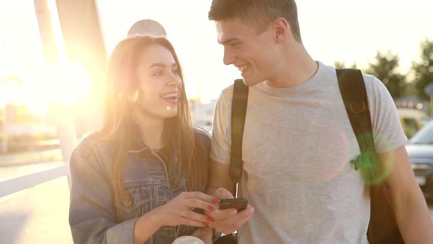 Young Attractive Couple Walking in the Street at Sunset. Using Modern Mobile Phone. Man Showing something on his Smartphone. Trendy Woman Smiling Happily. Looking Excited. Royalty-Free Stock Footage #1014030497