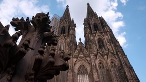 Camera slides past the Kreuzblume sculpture with the facade of Cologne Cathedral, Germany, behind.