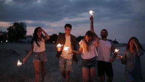 Friends walking, dancing and having fun during night party at the seaside with bengal sparkler lights in their hands. Young teenagers partying on the beach with fireworks. Slow motion steadycam shot. - Powered by Shutterstock - Get 15% off with code: PIKWIZARD15