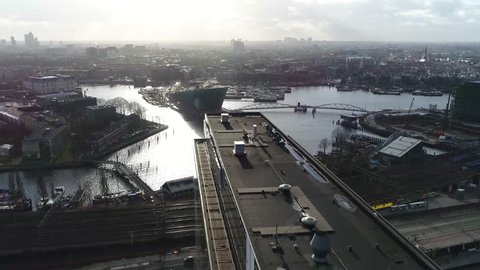 Aerial footage of Amsterdam city center moving over modern office building then showing Nieuwmarkt en Lastage neighbourhood NEMO Science Museum and The National Maritime Museum 4k high resolution