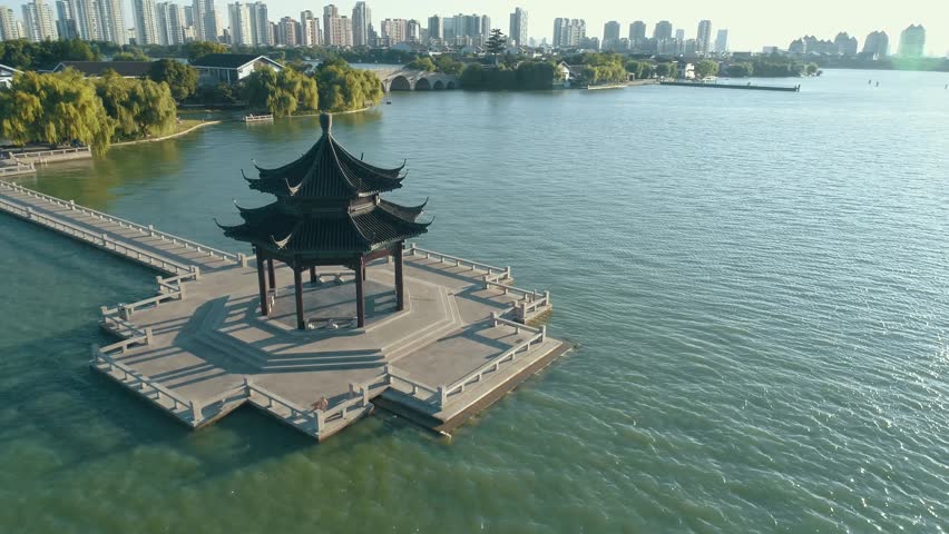 Aerial view over traditional chinese ancient pavilion on the lake on sunset, cityscape on the background
