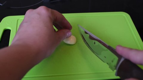 Grinding cloves of garlic for cooking, a knife on a green cutting Board
