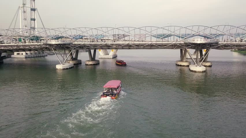 Aerial Shot Of A Tourist Boat Heading Under The Helix Bridge In Marina Bay Singapore At Sunset