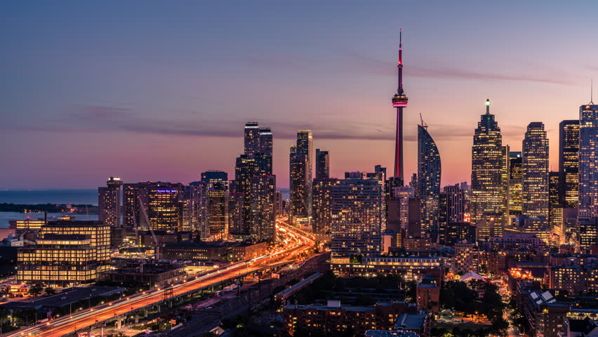 The historic Toronto Cn Tower in the midst of the entire downtown city skyline  with beautiful sunset with orange, red, and purple clouds along the horizon. 
