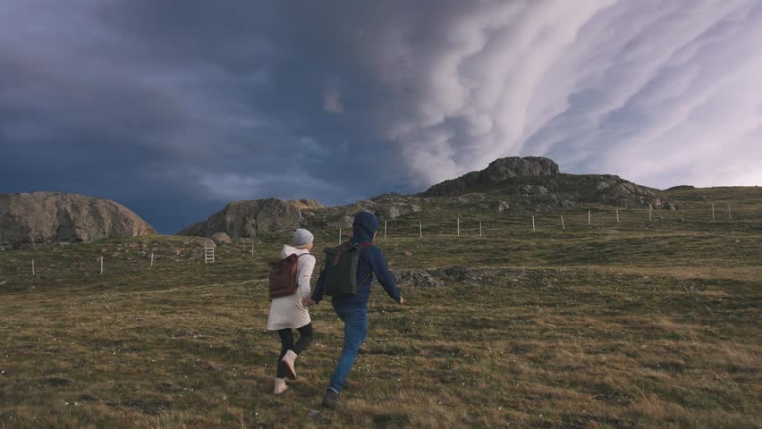Young loving couple running in field on background of epic dramatic clouds, slow motion
