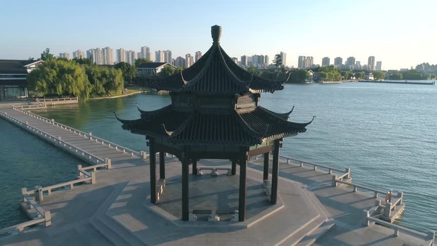 Aerial view over traditional chinese ancient pavilion on the lake on sunset, cityscape on the background