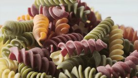 Dried colored fusilli pasta in wooden bowl on white board