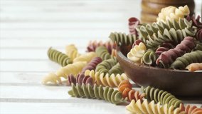 Dried colored fusilli pasta in wooden bowl on white board