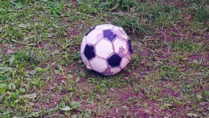 female legs in sneakers play with an old soccer ball on the grass