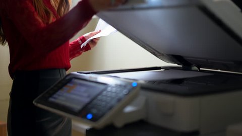 Young girl at office, pressing a button, turns on the printer and making copies of documents.