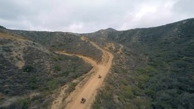 Aerial Drone view of motorcycles and ATV Sport Quad bikes riding on a dirt road through the mountains.  Tracking shot filmed in HD High Definition.