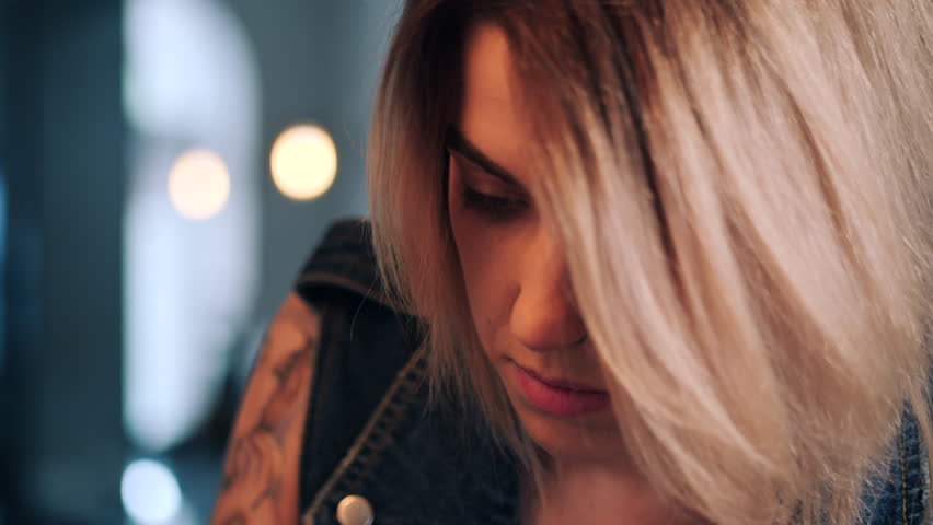 Young beautiful blonde woman portrait. Concentrated artist girl making tattoo with inks in her own studio. Close up working with gun machine. 4k.