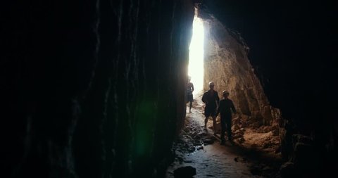 Group of young explorers in helmets enters to the dark cave Stock Video