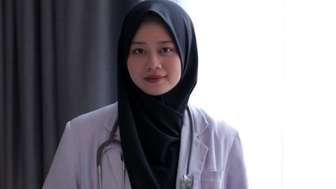 Close up portrait of asian muslim female doctor standing and smiling at camera at hospital. Edited and raw.
